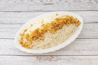 Tuzla kaynatılmış beyaz pirinç tepsisi ve açık renkli bir masanın üstünde çıtır çıtır soğan.