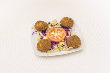 Küçük beyaz tabakta marul, mor lahana ve domates salatasıyla karıştırılmış falafel topları.