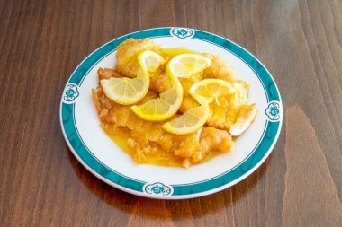 Breaded chicken fillets soaked in Chinese lemon sauce on white plate and brown wooden table
