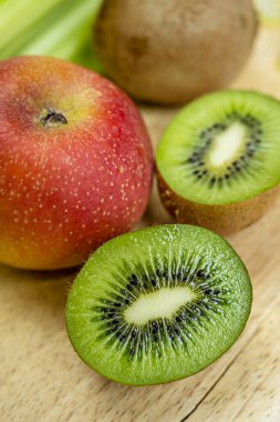 Yakın plan kivi kesimi ve arka planda daha fazla kivi ve açık ahşap arka planda kırmızı elma