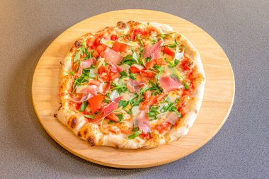 Spanish pizza with serrano ham and arugula with fine flour dough on round wooden board