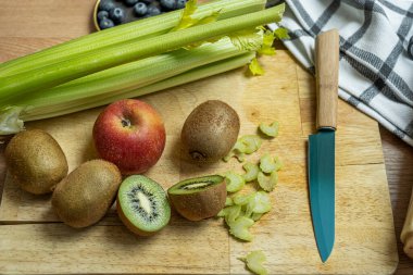 Kivi, elma, bir demet kereviz ve yabanmersini, sağlıklı bir antioksidan suyu yapmak için hazırlanmış kesme tahtasının üzerinde.