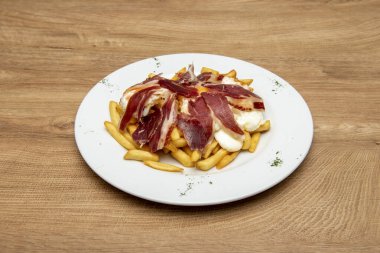 Kırık yumurtaları Serrano jambonu ve kızarmış patatesle paylaşmak için kapaklı yuvarlak tabak.