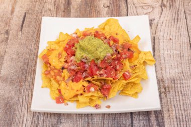 Bir tabak nachos, guacamole, çedar peyniri, doğranmış domates ve soslu soğan.