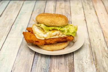 Yalnız hamburger, tavuk filetosu ve hamurlu yumurta, yanında marul ve tahtadan yapılmış susam tohumlu ekmek.