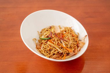 Turuncu masada taze sebze ve yakisoba soslu sotelenmiş erişte kasesi.