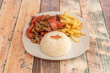 Bir tabak tipik Peru usulü biftek filetosu sebzeli ve soya soslu çift garnitürlü kızarmış patates ve beyaz pirinç.