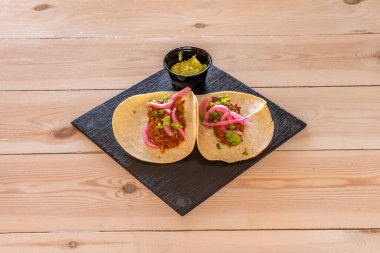 İki Meksika Cochinita Pibil Taco 'su ve bir kase guacamole. Tahta masa üzerinde siyah tahta tabakta.