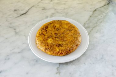 Beyaz mermer bir masada beyaz bir tabakta bol meyve suyu ile servis edilen İspanyol omleti.