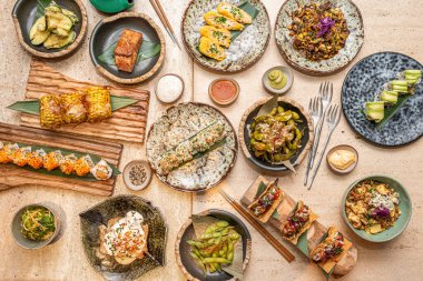 Misket masasında Asya yemekleri. edamame, California Roll, uramaki somon, deniz mahsulleri taco, soya sosu, susam, mısır, somon.