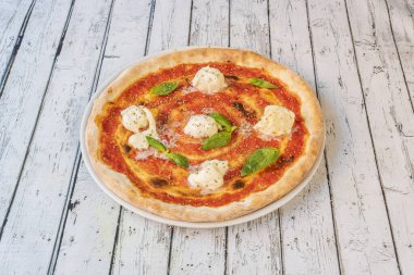 Kahvaltıda Margarita pizza. Graten peynirli toplar, domates ve fesleğen yapraklı beyaz masa.