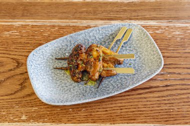 Kömürde ızgara tavuk kanadı şiş, zeytinyağı ile marine edilmiş mavi çay tabağı.