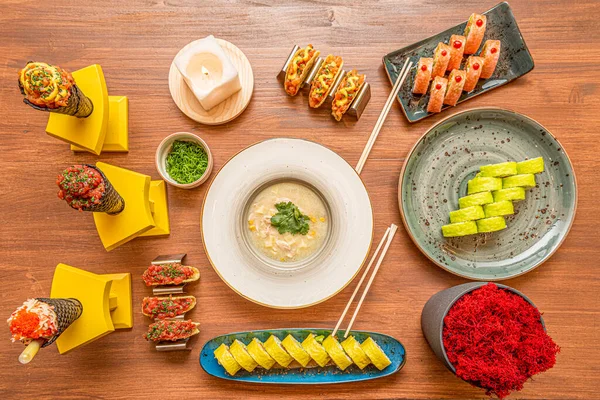 Set of fusion food dishes of various nationalities, tuna and salmon tartare in cones, soup of the day in the center, salmon and tuna tacos and sushi with seaweed substitutes
