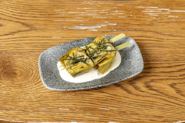 Gri tepside bir şişe şekerli enginar ve üzerinde kurutulmuş yosun var.