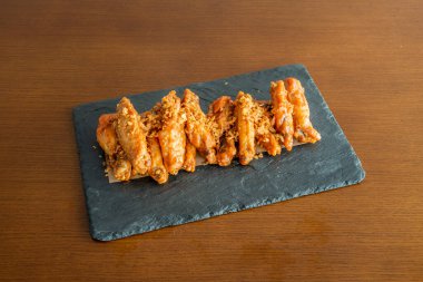 Barbekü ızgara tavuk kanadı ve siyah bir tabakta bol sos.