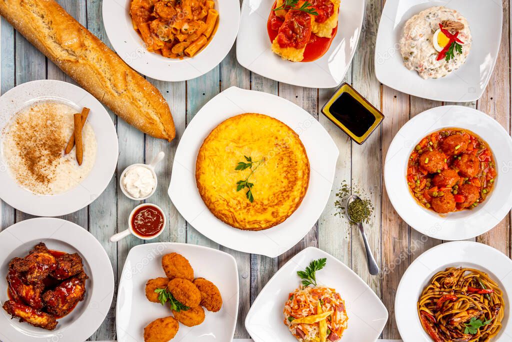 Set of popular food dishes in a Spanish tapas and fusion tavern. Russian salad, potato omelette, rice with milk, meatloaf in sauce, cod croquettes, barbecue wings.