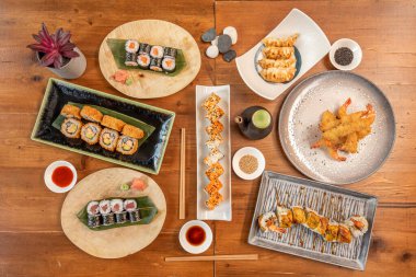 Japon yemek çubuklarının en üst görüntüsü. Tempura, California Roll, somon ve kırmızı ton balığı, kızarmış gyozas, soya sosu, susam tohumu, ejderha rulosu, muz yaprağı ve yemek çubuğu.