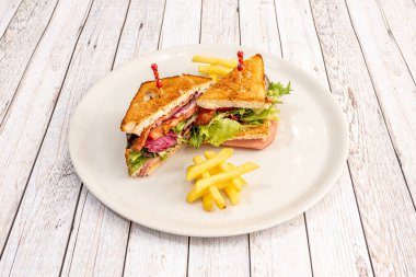 Typical club sandwich with layers of lettuce, sliced tomato, bacon, red onion, ham and grilled sliced bread