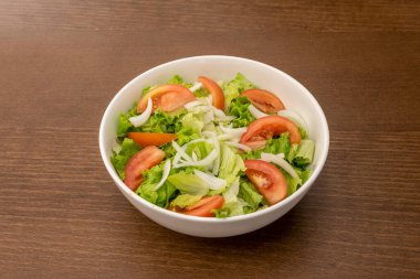 Bahçe salatası, doğranmış domates, marul ve beyaz soğanlı sade bir kâse ve ahşap masa.