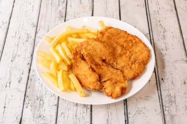 Zeytinyağında kızartılmış tavuk göğsü. Beyaz tabakta patates kızartmasıyla süslenmiş.