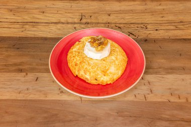 Büyük patates omleti, keçi peyniri ve kırmızı tabakta karamelize soğan ve ahşap masa.