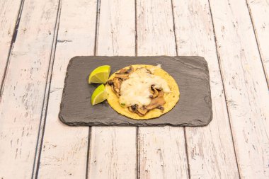 Mısır unlu tortilla üzerine erimiş peynirli kızarmış mantarlı taco ve yanında iki dilim limon.