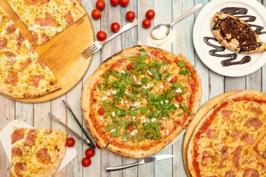 Bol roka, jambon ve York 'lu pizza ve erimiş peynir, çikolata soslu tatlı calzone, kiraz domatesleri, bıçaklar ve çatallar, guanciale pizzası.