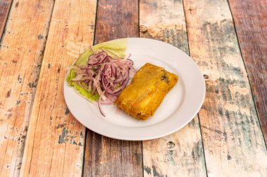 Kübalı et güveciyle doldurulmuş mısırlı tamale ve beyaz tabakta bir sürü çiğ mor soğan.