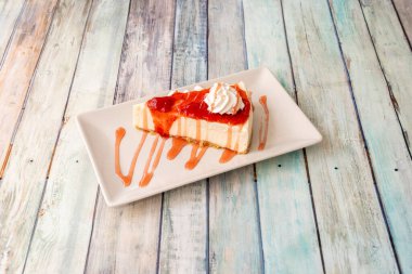 Çilek reçelli cheesecake porsiyonu. Biraz krema ve beyaz tabakta çilek şurubu.