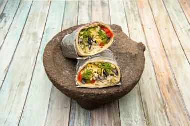 Büyük burrito, yarı yarıya, alüminyum folyoya sarılmış, yeşil sucukla doldurulmuş, siyah fasulye, ve volkanik taş üzerinde peynirli pilav.