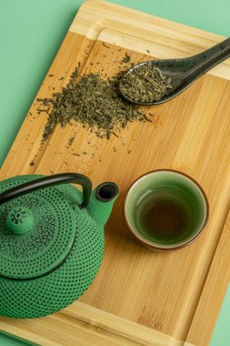 Geleneksel yeşil çay seti ve koyu bambu masasında kuru çay ve yeşil arka planda siyah porselen kaşık.