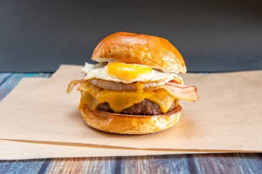 Bol peynirli sığır burger, beyaz soğan dilimleri, kızarmış domuz pastırması ve yumurta sarısını kahverengi gıda kağıdına batırmak için.