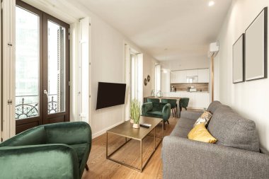 Yeşil kadife koltukları, duvar kliması ve büyük pencereleri olan kiralık bir tatil dairesinde televizyonlu oturma odası.