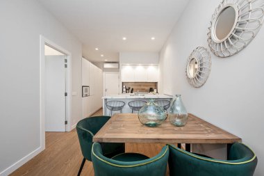 Güzel ahşap yemek masası yeşil kadife döşemeli sandalyeler, çağdaş dekor ve mutfak adası ve arka planda modern mutfak. Yepyeni bir kiralık tatil dairesi..