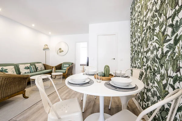 Small round white dining table with service set surrounded by decorative accessories similar to plants and leaves in a vacation rental apartment