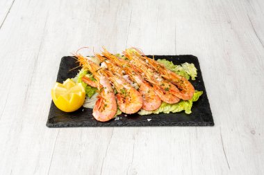 Izgarada Cadiz 'den büyük porsiyon kızarmış karides ve limon suyu, doğranmış maydanoz ve siyah bir tabakta tuz taneleri ile marul yatağı gönderin.