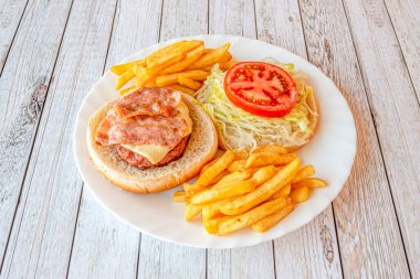 Hamburger tabakta, olgun domates salatası ve buzdağında salata üzerine erimiş trans peynirli marul üzerine kızarmış domuz pastırması ve bolca patates kızartması.