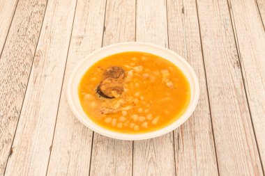 First plate of typical Spanish food of popular fabada with white beans stewed with verdura, meats and sausages of the country on wooden table