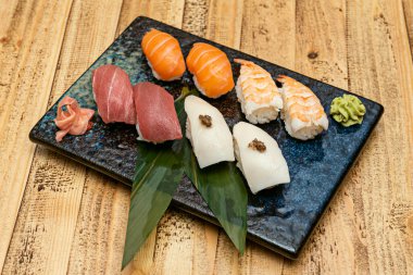 Muz yapraklı güzel siyah tepsi ve tipik Japon tereyağlı nigiri tarifi trüf, karides nigiri, Norveç somon nigiri ve ginseng ve wasabi ile almadraba 'dan kırmızı ton balığı.