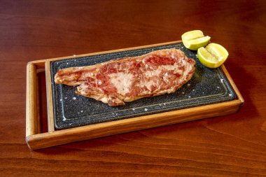great beef entrecote served on the same hot plate with wood protection with sea salt flakes and lemon wedges
