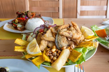 Peru usulü jalea tarifi. İçinde çeşitli ezilmiş balık, haşlanmış karides ve midye, mor soğan, farklı türde mısır, kızarmış yukka ve kızarmış muz var.