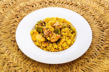 Geleneksel hasır masa örtüsü üzerinde sebze ve sürahi ile klasik Valencia usulü tavuk paella.