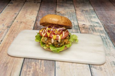 Şefin elleri domates ve marul üzerine peynirli ve pastırmalı hamburgerleri birleştiriyor.