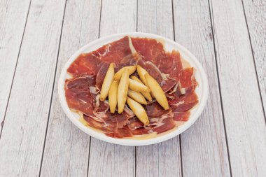 Beyaz tabak ve ince dilimli meşe palamudu ile beslenmiş İber jambonu.