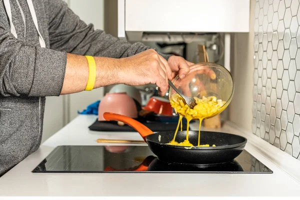 Man\'s hands pouring potatoes and beaten eggs into a non-stick frying pan to make a Spanish potato omelette