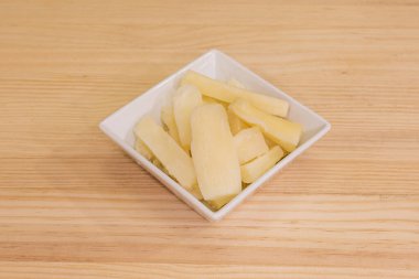 Beyaz kare kase ahşap masada kızarmış yukka parçaları ile dolu.