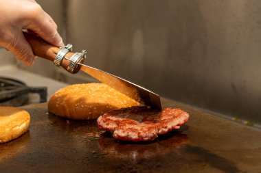 Şefin sol eli bir restoranda ızgara hamburger pişirmek için bir spatulayı tutuyor.