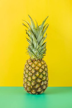 Sade yeşil masada olgun ananas ve parlak sarı zemin.