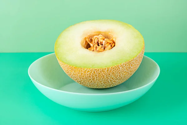 half ripe Galia melon with the seeds inside on a blue deep plate and plain green backgrounds