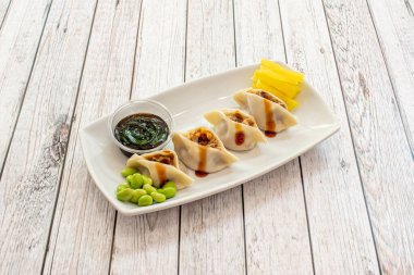 Soya soslu Asya hamur tatlısı ve edamame fasulyesi, beyaz tepside rendelenmiş sarı biber.